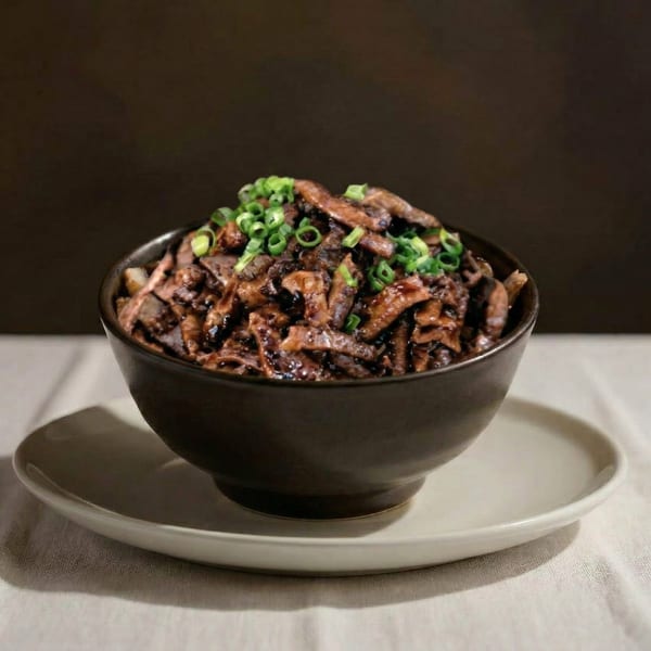A dark bowl of saucy beef strips topped with chopped green onions, on a white plate.