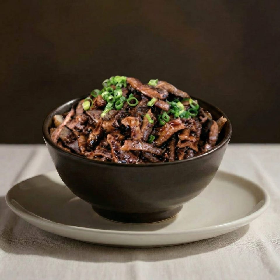 A dark bowl of saucy beef strips topped with chopped green onions, on a white plate.