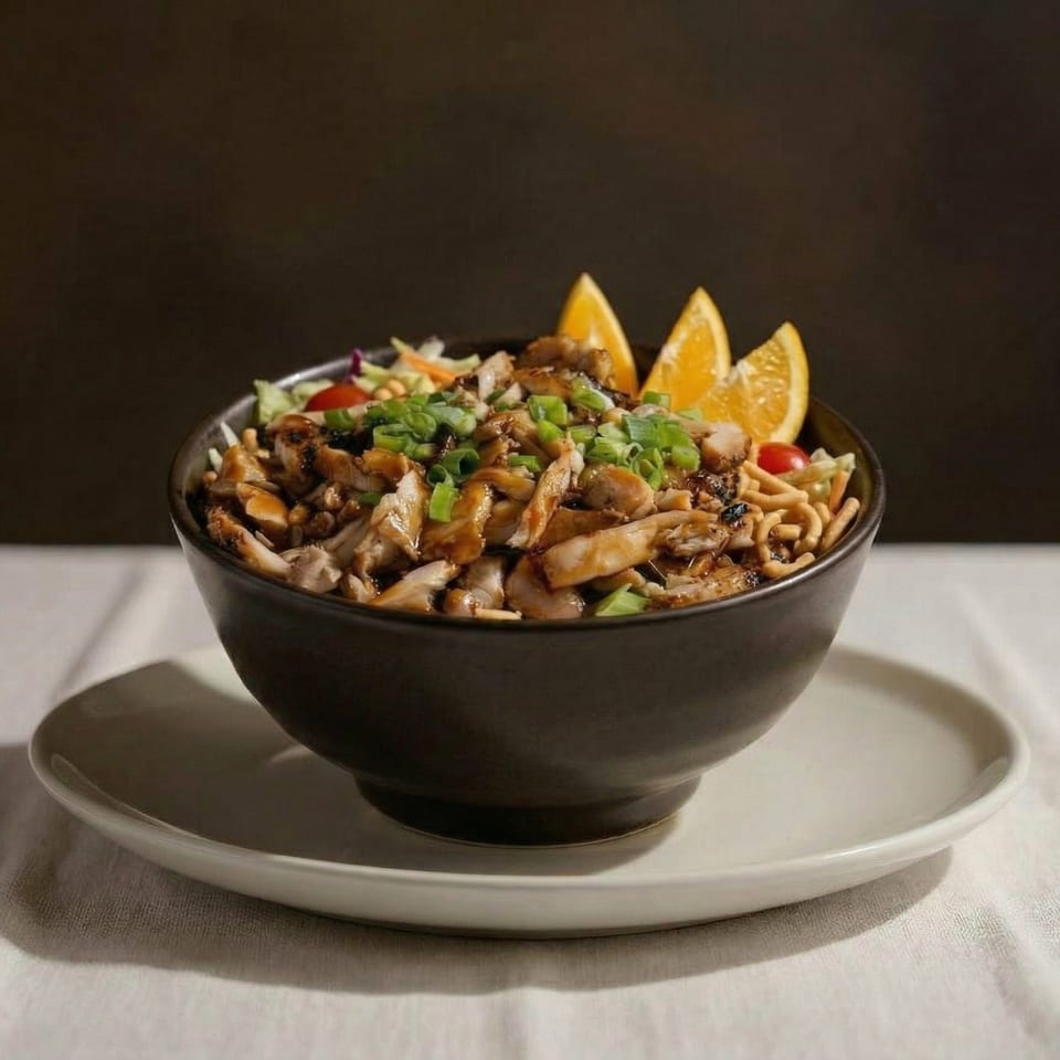 Teriyaki chicken bowl with oranges, noodles, and green onions on a white tablecloth.