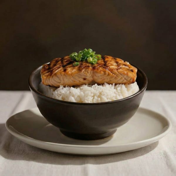 Grilled salmon with green onions on a bed of white rice in a dark bowl, on a light plate.